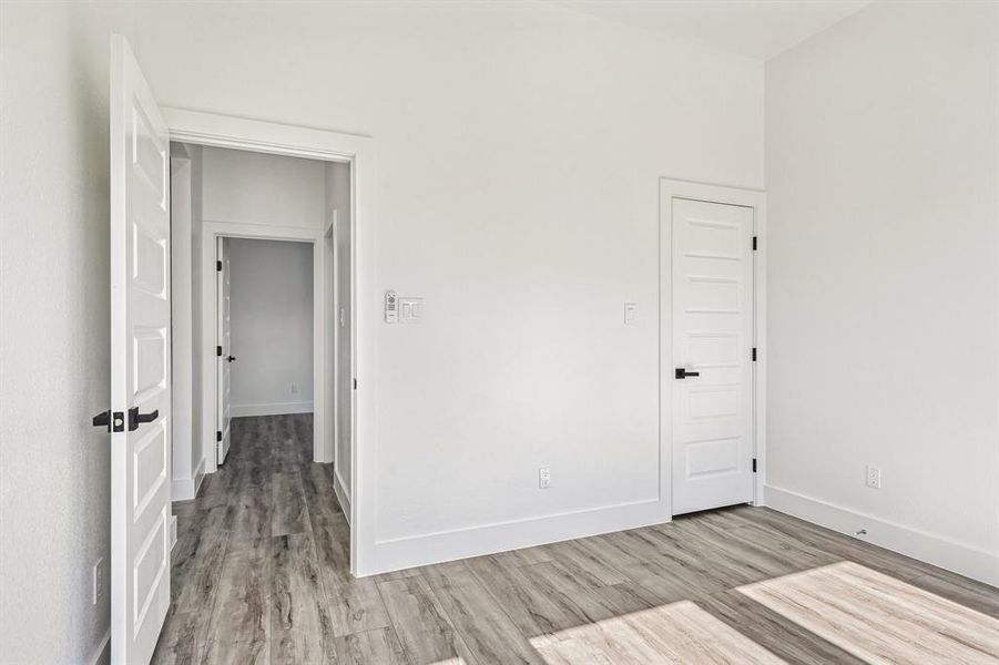 Room featuring wood-finish flooring, crisp white walls, white baseboards, and white paneled doors with black hardware