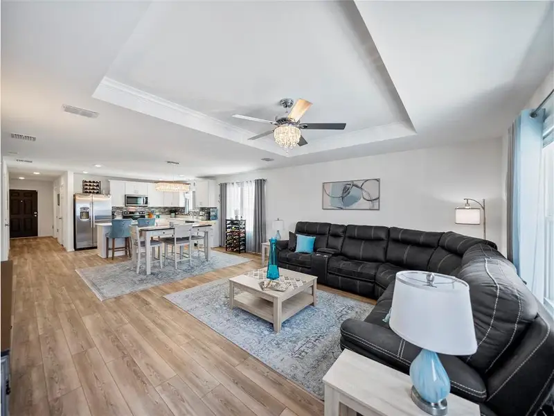 Living area with light wood-type flooring, a tray ceiling, visible vents, and ceiling fan