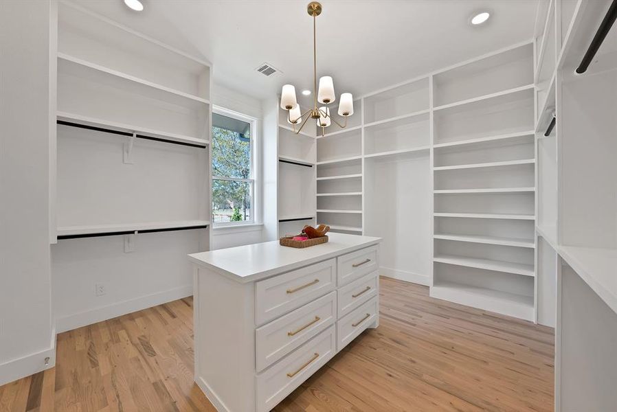 Spacious closet with light wood-type flooring and a chandelier