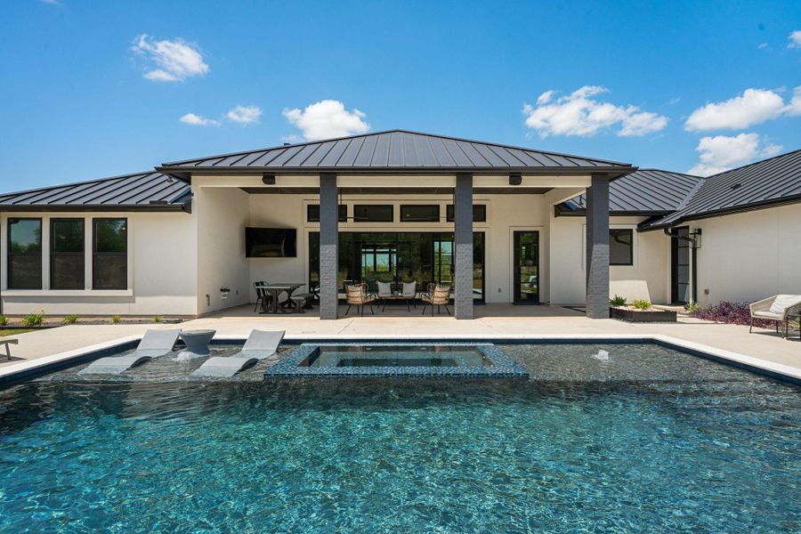 A dark metal roof crowns this modern residence bordering a custom pool and spa.