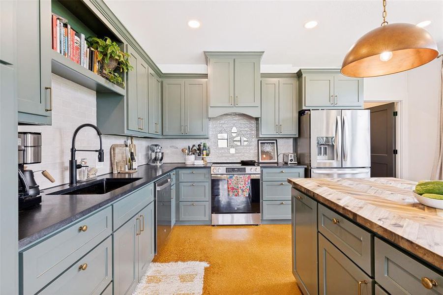 Modern kitchen featuring light green cabinetry, dark countertops, and a white subway tile backsplash Modern kitchen featuring light green cabinetry, dark countertops, and a white subway tile backsplash