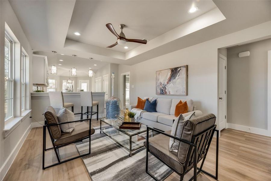 Living room featuring ceiling fan, light wood-type flooring, and a tray ceiling