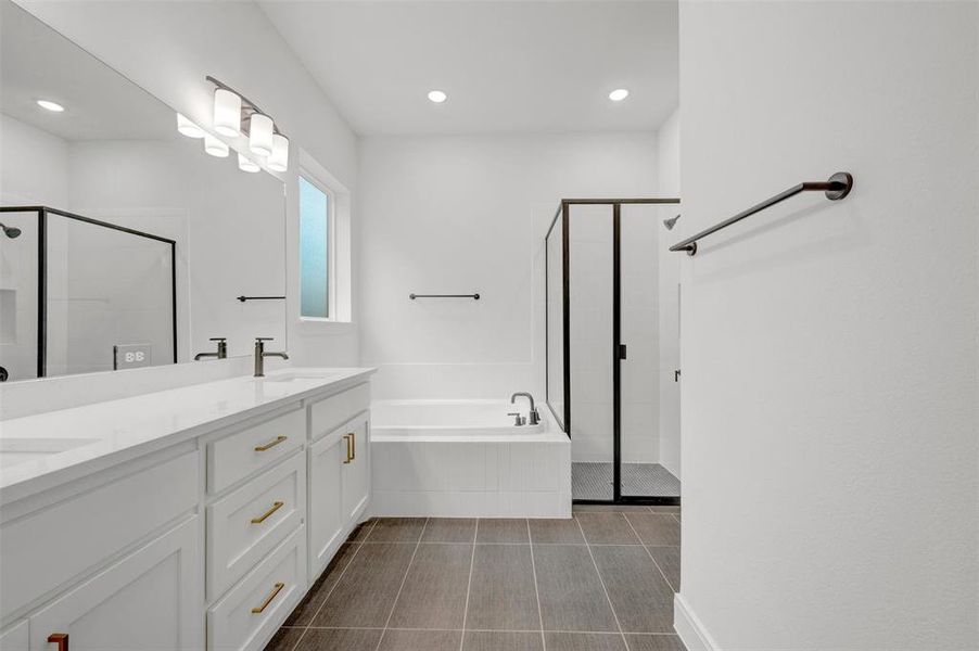 The bathroom features a double vanity with white cabinetry and gold hardware, a large soaking tub, a shower with black-framed glass, and recessed lighting