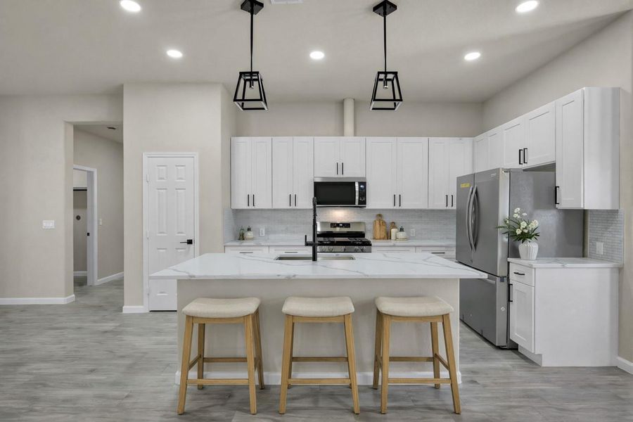 Gourmet kitchen view featuring stainless steel appliances, a deep undermount sink with a high-neck faucet, and beautiful stone-patterned countertops. Virtually staged