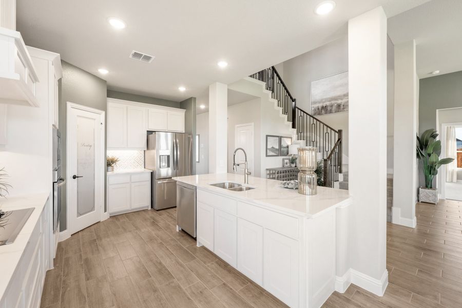 Kitchen with white cabinets, quartz island with sink, stainless steel appliances, and wood-look floors open to staircase