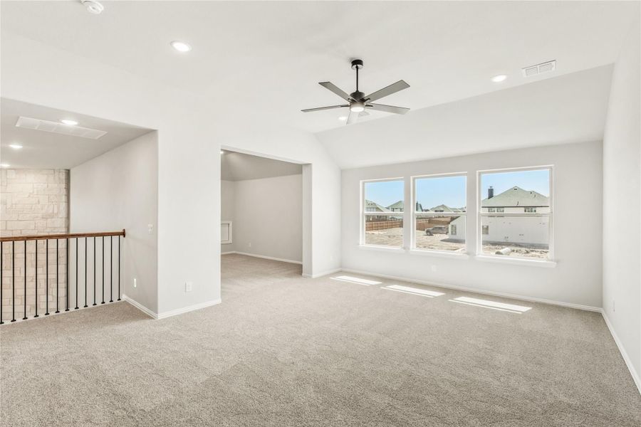 Open upstairs living area with carpet, ceiling fan, vaulted ceiling, and large windows overlooking neighboring homes Open upstairs living area with carpet, ceiling fan, vaulted ceiling, and large windows overlooking neighboring homes