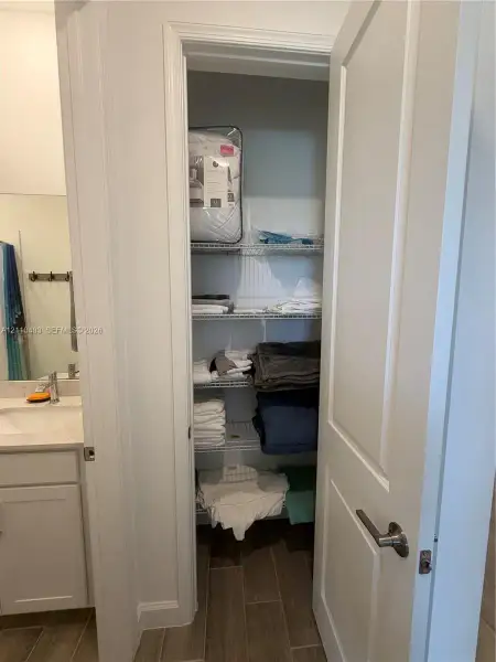 Storage closet featuring wire shelving, white panel door with brushed metal hardware, and wood-finish tile flooring