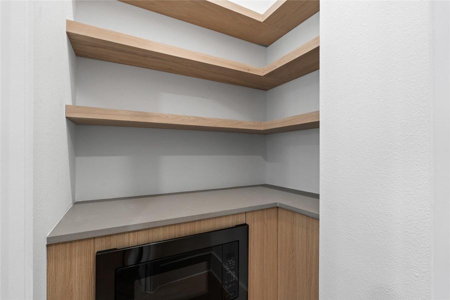 This pantry reads less utilitarian and more architectural—warm wood shelving layered above clean countertops creates an orderly backdrop for everyday rituals.