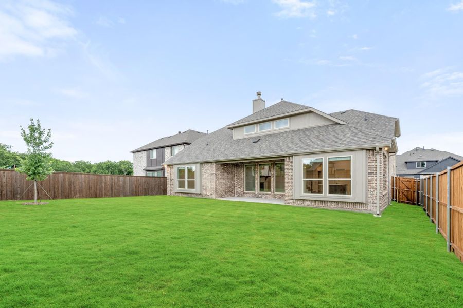 Rear view of two-story brick home with large fenced backyard and green lawn Rear view of two-story brick home with large fenced backyard and green lawn