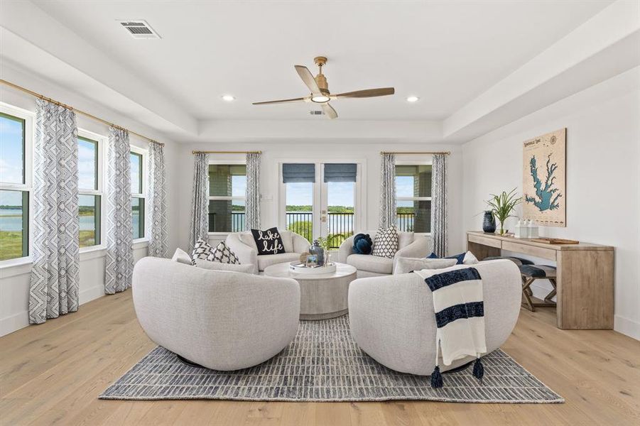 Living room with a raised ceiling, light wood-style flooring, ceiling fan, and recessed lighting Living room with a raised ceiling, light wood-style flooring, ceiling fan, and recessed lighting