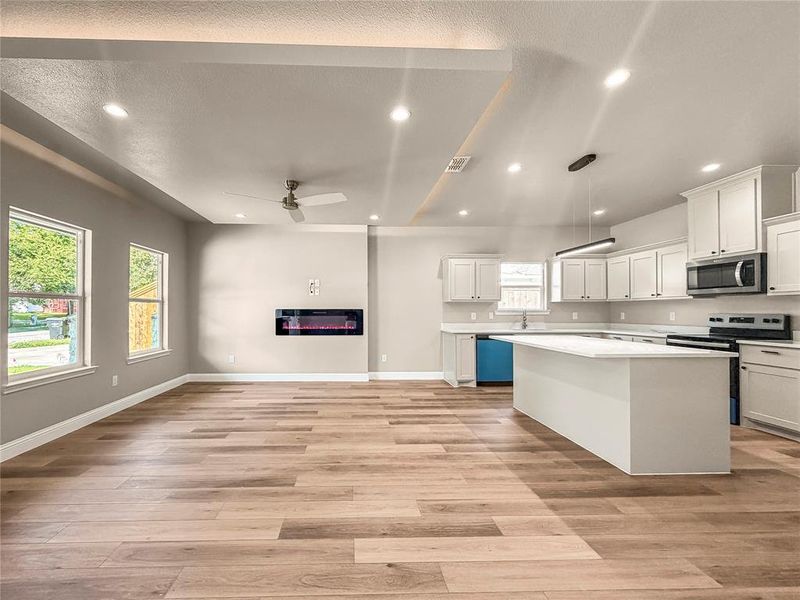 Open-concept living space featuring wood-finish flooring, recessed lighting, and an electric fireplace Open-concept living space featuring wood-finish flooring, recessed lighting, and an electric fireplace