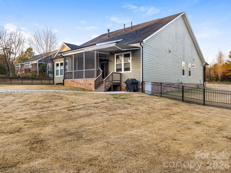 Backyard showing retractable awning over windows and gas stub-out for a grill/kitchen area.  View from inside the fenced yard (right side).