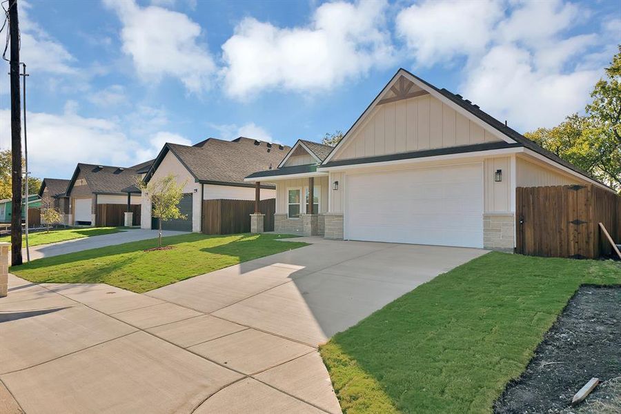 View of front facade with driveway, stone siding, board and batten siding, an attached garage, and a gate