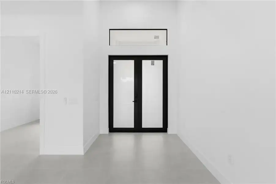 Double front doors featuring matte black frames with glass panel inserts, complemented by a rectangular transom window and large-format tile flooring