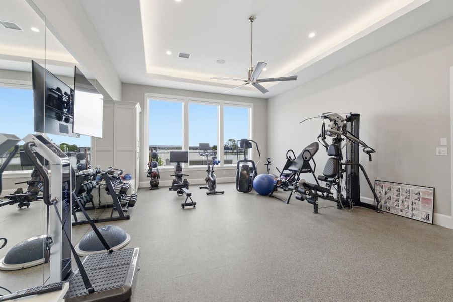 Exercise room featuring a ceiling fan, a raised ceiling, and recessed lighting