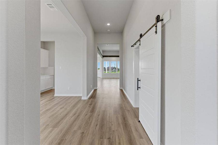 Inviting hallway with light wood-style flooring, leading to open living areas with large windows, and a modern white barn door with black hardware