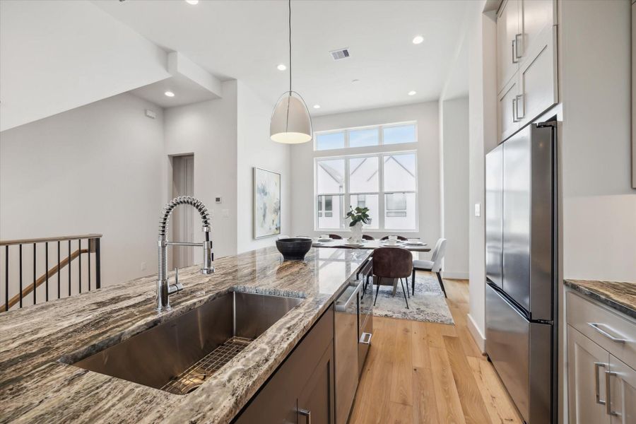 This modern kitchen features a spacious open layout with a large island, sleek marble countertops, and stainless steel appliances. Natural light floods the space through large windows, enhancing its bright and inviting atmosphere.