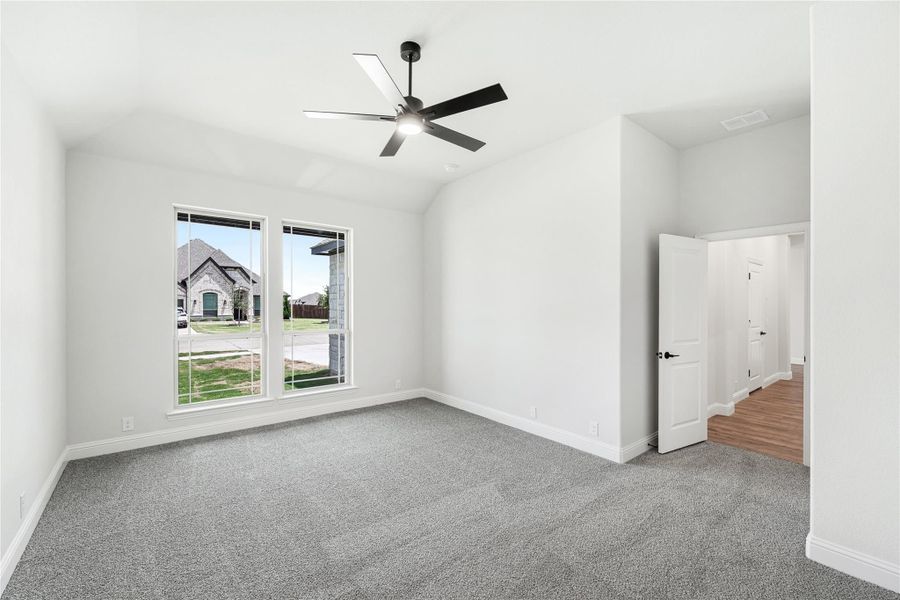 Empty bedroom with gray carpet, vaulted ceiling, black ceiling fan, and two windows