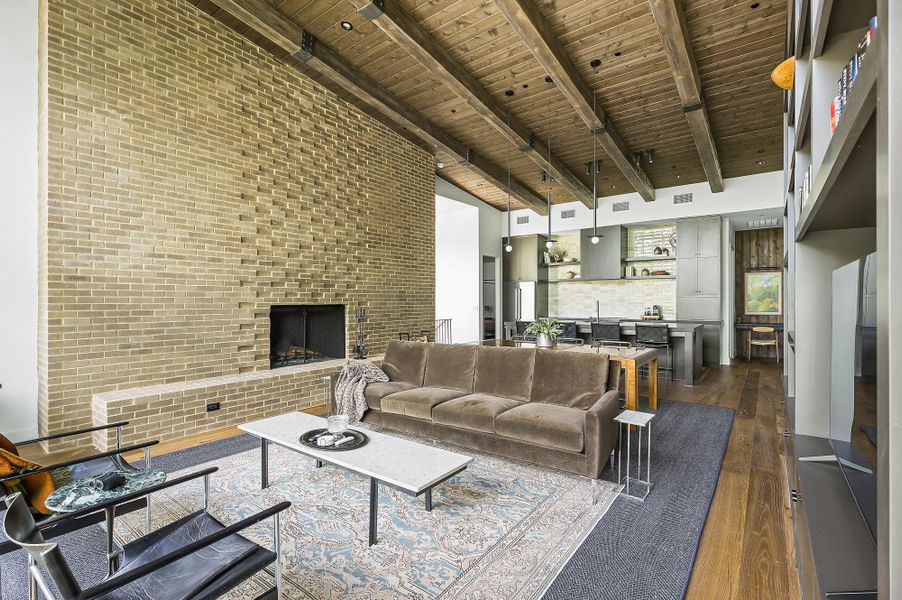 Living area featuring high vaulted ceiling, a wood ceiling with exposed beams, dark wood-type flooring, a fireplace, and brick wall Living area featuring high vaulted ceiling, a wood ceiling with exposed beams, dark wood-type flooring, a fireplace, and brick wall