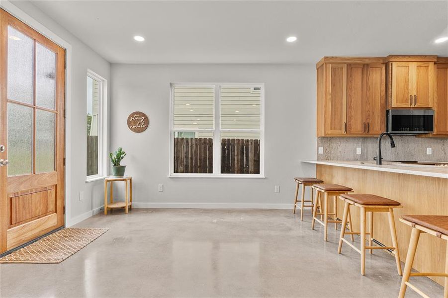 Kitchen with concrete floors, decorative backsplash, a breakfast bar, recessed lighting, and brown cabinetry Kitchen with concrete floors, decorative backsplash, a breakfast bar, recessed lighting, and brown cabinetry