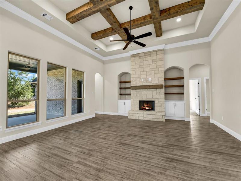 Unfurnished living room with coffered ceiling, ceiling fan, built in features, a fireplace, and beamed ceiling