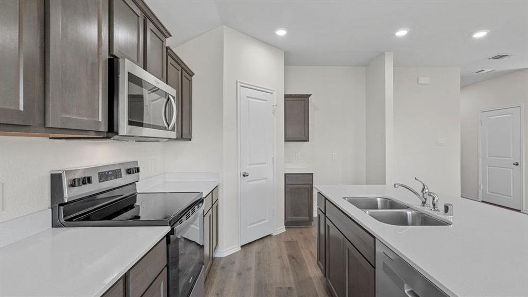 Kitchen featuring stainless steel appliances, wood finished floors, recessed lighting, light stone counters, and dark wood finish cabinets