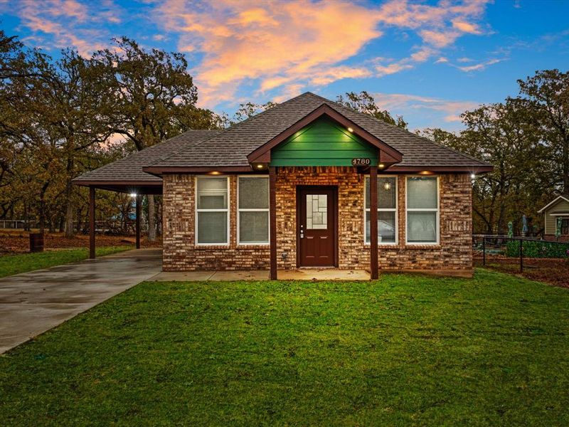 View of front of home with a front yard, driveway, a carport, and brick siding