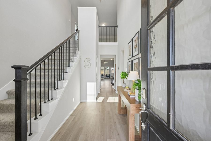 Step into a bright and inviting foyer with sleek wood-look floors, a stylish staircase, and elegant decor leading the way to an open and airy living space.