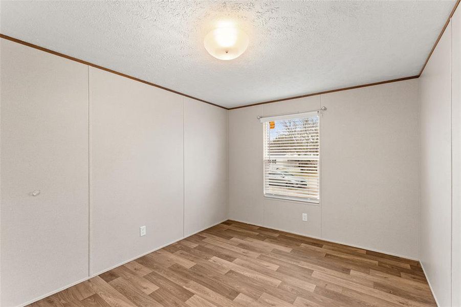Unfurnished room featuring light wood-style flooring, crown molding, and a textured ceiling