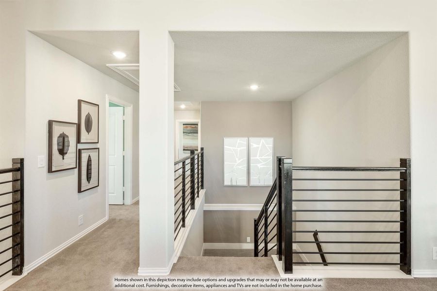 Upper hallway with black metal horizontal railings, carpet flooring, and framed wall art near staircase