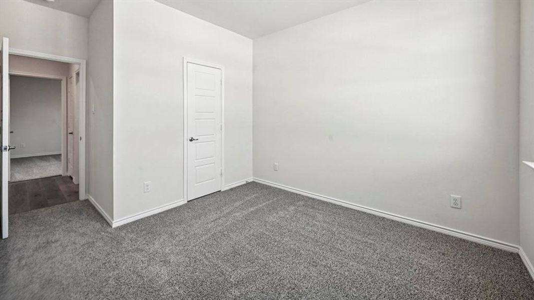 Spacious room featuring gray speckled carpeting, white baseboards, and a five-panel interior door with matte black hardware