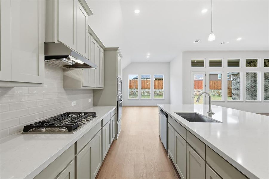 Kitchen featuring decorative light fixtures, light wood finished floors, light stone countertops, stainless steel appliances, and gray cabinetry
