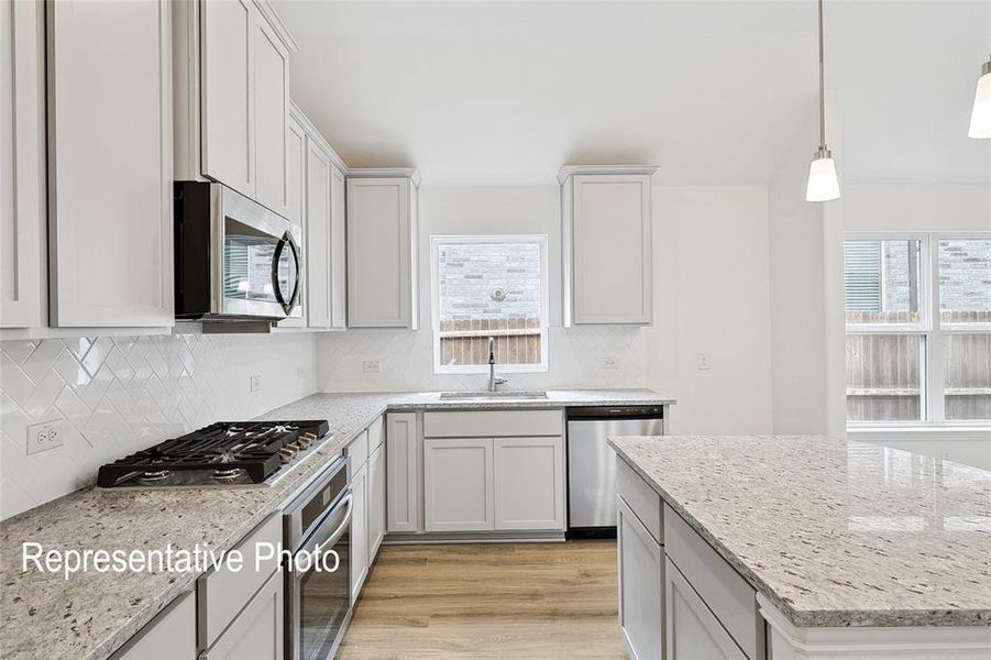 Kitchen featuring light-finish cabinetry, speckled countertops, herringbone tile backsplash, and wood-finish flooring