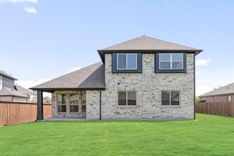 Two-story brick home rear view with covered patio, large backyard, and wood privacy fence Two-story brick home rear view with covered patio, large backyard, and wood privacy fence