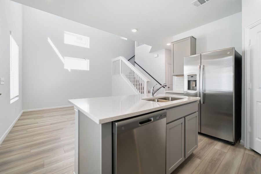 Kitchen with stainless steel appliances, gray cabinetry, a kitchen island with sink, light stone countertops, and light wood-style floors