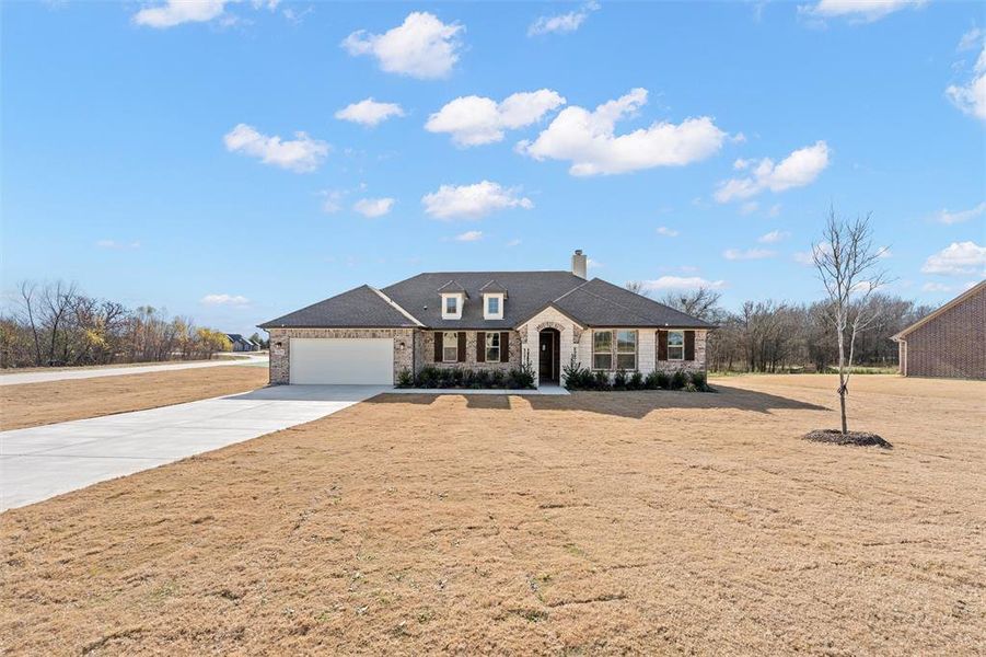 View of front facade featuring concrete driveway, a chimney, an attached garage, stone siding, and a front lawn
