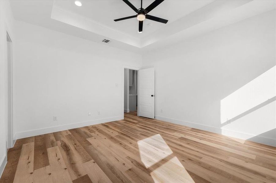 Unfurnished bedroom with a raised ceiling, ceiling fan, a towering ceiling, and light wood-type flooring