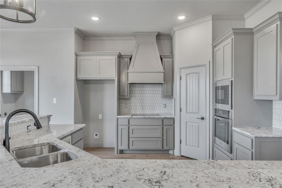 Kitchen featuring premium range hood, sink, gray cabinets, appliances with stainless steel finishes, and decorative backsplash