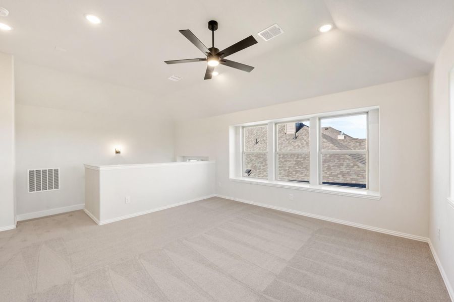 Empty bedroom with vaulted ceiling, ceiling fan, carpet flooring, and large triple window