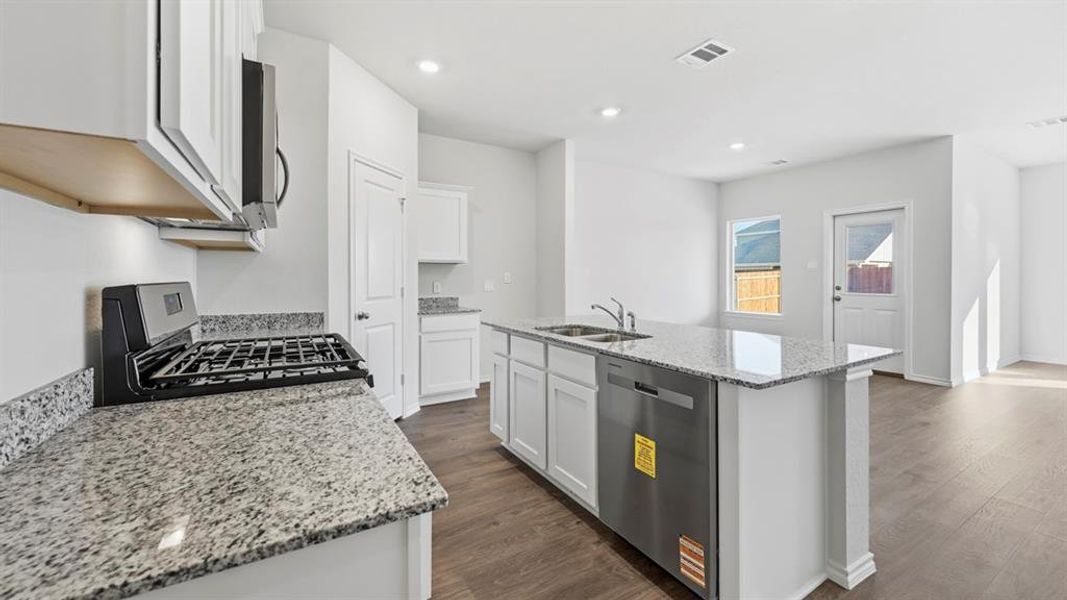 Kitchen with light stone countertops, dishwasher, range with gas stovetop, a center island with sink, and dark wood finished floors