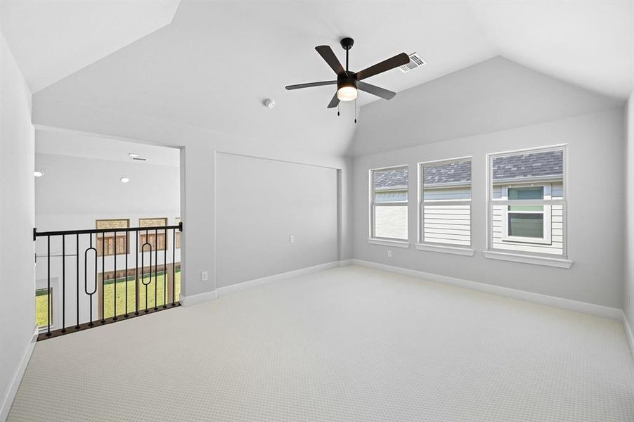 Empty room with vaulted ceiling, healthy amount of natural light, carpet flooring, and a ceiling fan