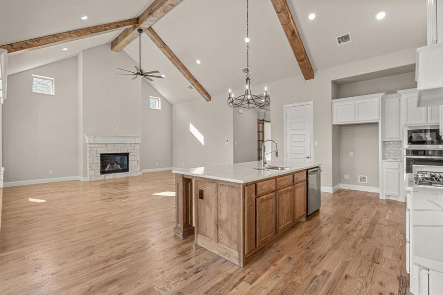 Kitchen featuring light stone counters, white cabinets, built in microwave, stainless steel dishwasher, and a large island with sink