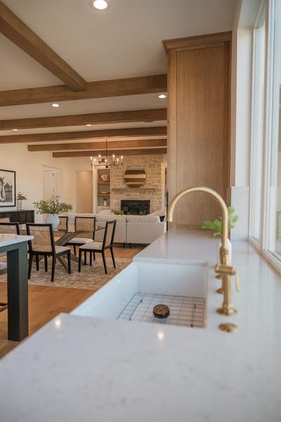 Kitchen with a fireplace, light wood finished floors, beam ceiling, open floor plan, and hanging lights Kitchen with a fireplace, light wood finished floors, beam ceiling, open floor plan, and hanging lights