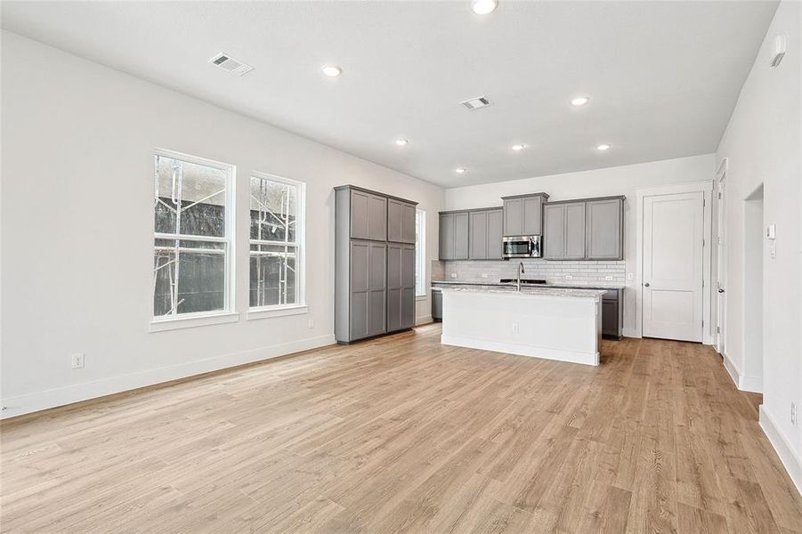 Kitchen with light hardwood / wood-style floors, decorative backsplash, a kitchen island with sink, and gray cabinets