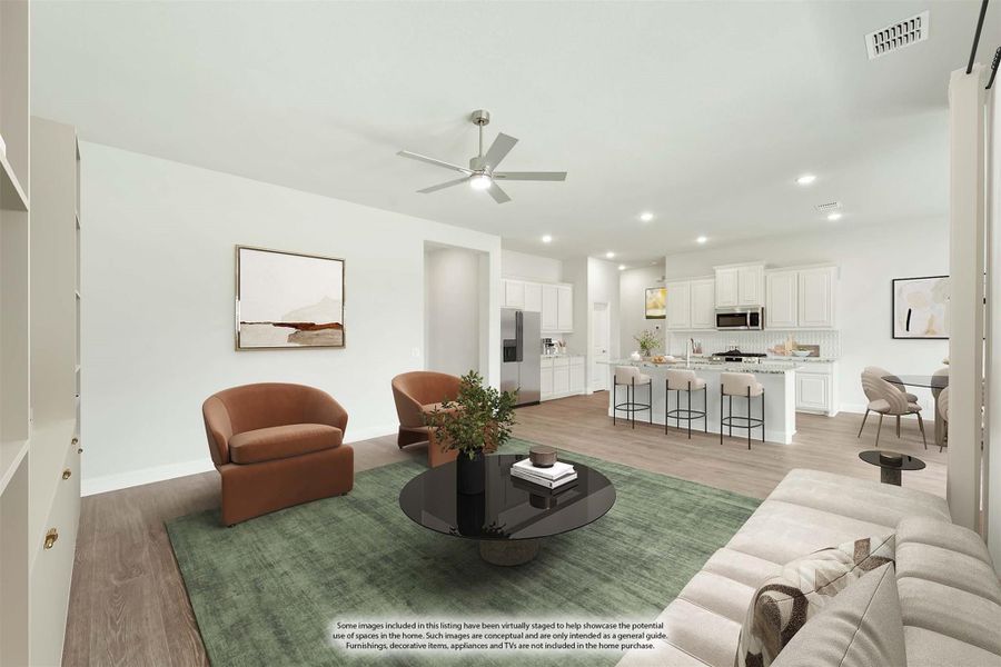 Open-concept living room with ceiling fan and hardwood floors, open to white kitchen with island and bar seating Open-concept living room with ceiling fan and hardwood floors, open to white kitchen with island and bar seating