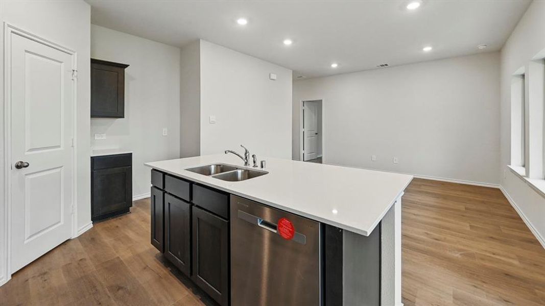 Kitchen with recessed lighting, a center island with sink, stainless steel dishwasher, dark wood-style flooring, and light stone counters