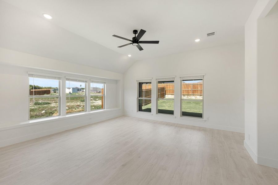 Empty living room with vaulted ceiling, black ceiling fan, light wood floors, and large windows
