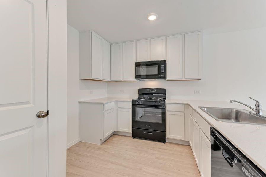 Kitchen with a sink, white cabinets, light countertops, black appliances, and light wood finished floors