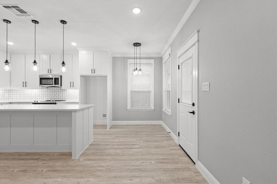 Kitchen with light wood-type flooring, white cabinetry, pendant lighting, tasteful backsplash, and ornamental molding