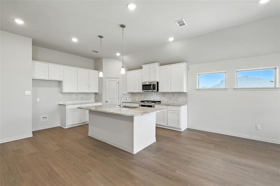 Kitchen featuring backsplash, white cabinetry, an island with sink, light stone countertops, and recessed lighting Kitchen featuring backsplash, white cabinetry, an island with sink, light stone countertops, and recessed lighting